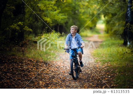 Teen boy rides a bicycle along a path in the forest. The cyclist rides fast through the springboards. Teen boy rides a bicycle along a path in the forest. The cyclist rides fast through the springboards. 61313535