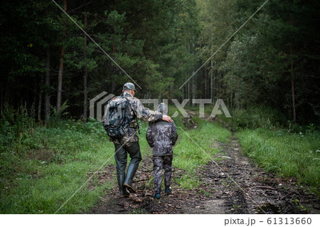 Hunters with hunting equipment going away through rural field towards forest at sunset during hunting season in countryside. Hunters with hunting equipment going away through rural field towards forest at sunset during hunting season in countryside. 61313660