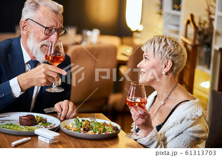 Stylish senior couple taking meal in restaurant, using electronic cigarette. IQOS 61313703