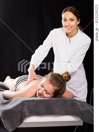 female masseur doing massage at back young woman, who lying on a massage table in a beauty salon female masseur doing massage at back young woman, who lying on a massage table in a beauty salon 61320325