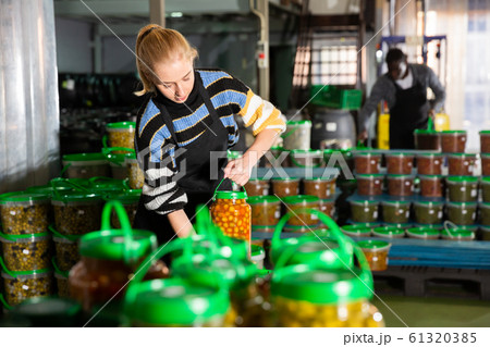 Woman stacking glass jars with pickled olives 61320385