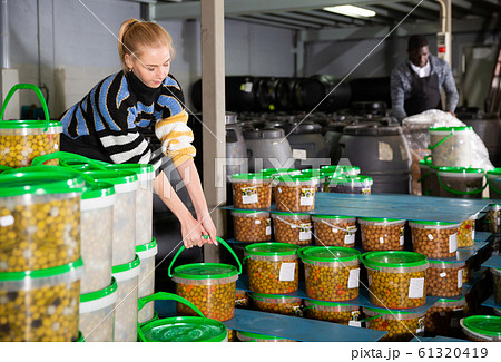 Workwoman stacking plastic buckets with olives 61320419