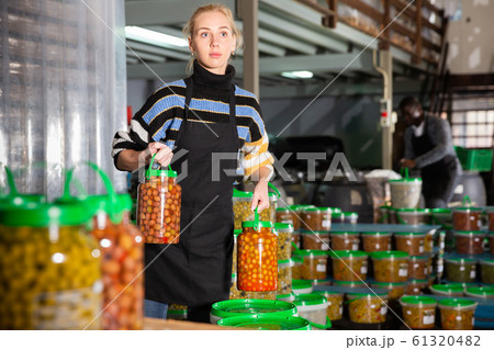 Female worker stocks plastic containers and cans with olives in warehouse Female worker stocks plastic containers and cans with olives in warehouse 61320482