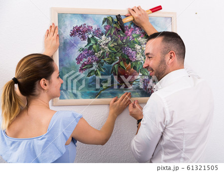 Man is hanging the picture on the wall together with his wife Man is hanging the picture on the wall together with his wife 61321505
