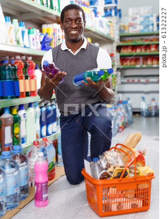 joyous African man holding bottle of household chemicals in store 61322227