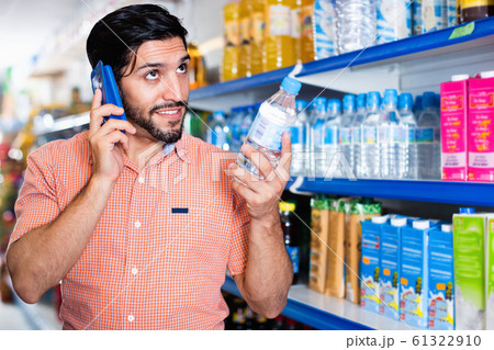 Man is choosing water with help mobile in supermarket. 61322910