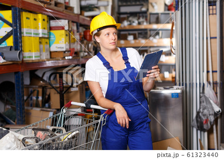 Young woman customer in helmet with notebook looking construction materials Young woman customer in helmet with notebook looking construction materials 61323440