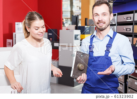 Smiling salesman offering door lock to young woman in shop 61323902