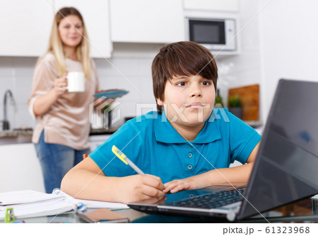 Boy doing homework, mother cooking Boy doing homework, mother cooking 61323968
