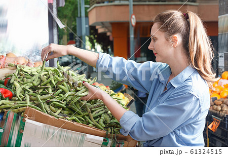 Female is choosing peas on the shelves in the market. 61324515