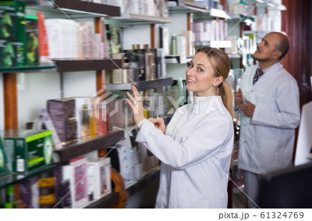 Smiling pharmacists standing next to shelves 61324769