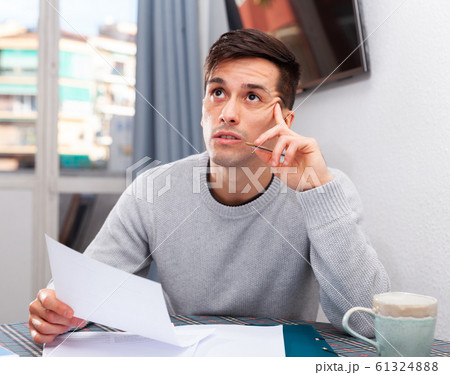 Man sitting at table at home calculating domestic finances and bills Man sitting at table at home calculating domestic finances and bills 61324888