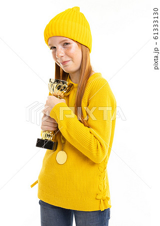 Happy teenager girl with red hair, yellow hoody and trousers holds a gold cup isolated on white Happy teenager girl with red hair, yellow hoody and trousers holds a gold cup isolated on white 61333130