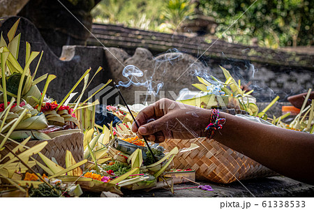 A hand placing burning incense in an offering at a Balinese temple 61338533