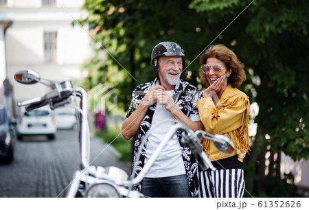 A cheerful senior couple travellers with motorbike in town. A cheerful senior couple travellers with motorbike in town. 61352626