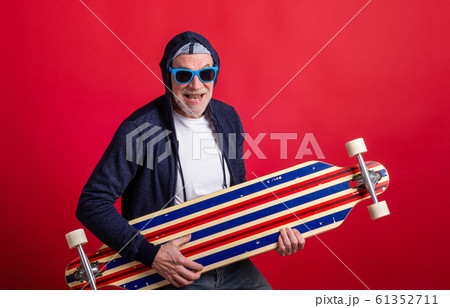 A senior man with longboard in a studio on red background, looking at camera. A senior man with longboard in a studio on red background, looking at camera. 61352711