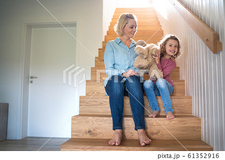 A cute small girl with mother indoors at home, sitting on staircase. 61352916