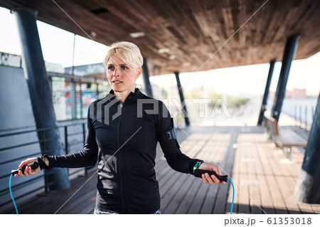 A young sportswoman doing exercise outdoors, skipping. A young sportswoman doing exercise outdoors, skipping. 61353018