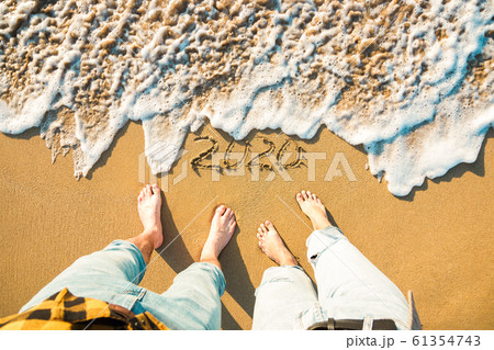 Top view legs of a couple on sandy beach and year 2020 on it, wave approaching 61354743