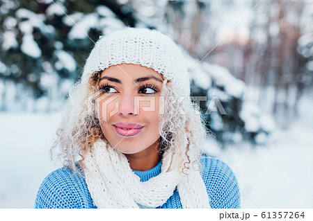 portrait of young afro american girl wearing hat, blue sweater posing in winter park. portrait of young afro american girl wearing hat, blue sweater posing in winter park. 61357264