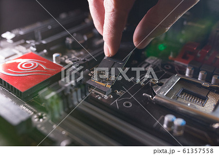 Focus at SSD slot, type M.2 with support for NVMe, on computer motherboard. Technician is installing new fast high capacity drive with flash chips, known as SSD. Focus at SSD slot, type M.2 with support for NVMe, on computer motherboard. Technician is installing new fast high capacity drive with flash chips, known as SSD. 61357558