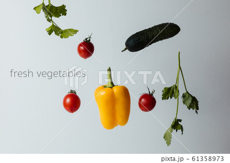 Healthy salad with flying vegetable ingredients on a white background. Cherry tomatoes, yellow pepper, cucumber, parsley 61358973