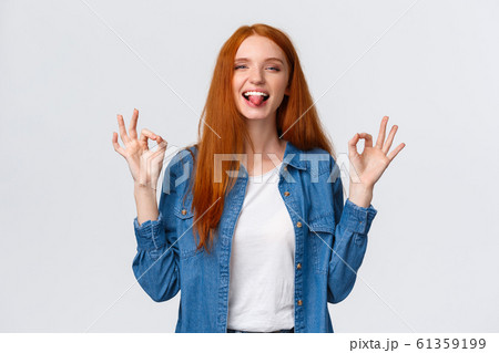 Relaxed and carefree, positive redhead girl chilling on party, having fun leisure weekends, showing okay gestures calming down, assuring all good, showing tongue and smiling playful 61359199