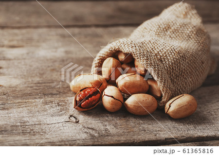 Pecans are spilled out of a burlap bag onto a Pecans are spilled out of a burlap bag onto a 61365816