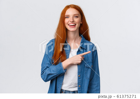 Carefree, friendly and happy outgoing redhead woman in denim shirt, pointing finger right and laughing at camera with beaming smile, standing white background, having discussion, communicate team 61375271