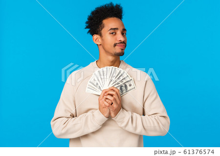 Suspicious and doubtful young pensive african-american rich guy holding big cash, lottery prize, have money and looking with disbelief or skeptical camera, unwilling share, standing blue background Suspicious and doubtful young pensive african-american rich guy holding big cash, lottery prize, have money and looking with disbelief or skeptical camera, unwilling share, standing blue background 61376574