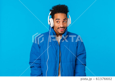 Technology, modern lifestyle and gadgets concept. Cheerful attractive hipster african american guy walking winter snowy streets, wearing padded jacket and headphones, listen music 61376602