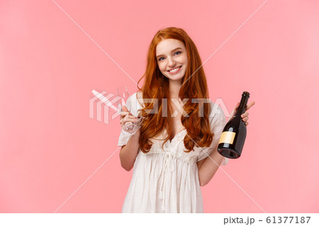 Relationship, celebration and tenderness concept. Lovely caucasian girl with red long curly hair in white dress, inviting have drink together, holding champagne and two glasses, smiling 61377187
