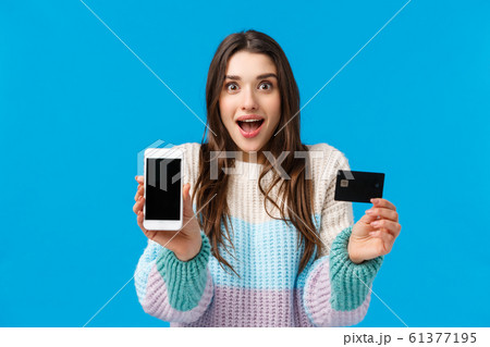 Smiling, excited and fascinated young woman talking about cool new app, banking application, deposit or cashback service, holding smartphone facing display camera, credit card, grinning amused Smiling, excited and fascinated young woman talking about cool new app, banking application, deposit or cashback service, holding smartphone facing display camera, credit card, grinning amused 61377195