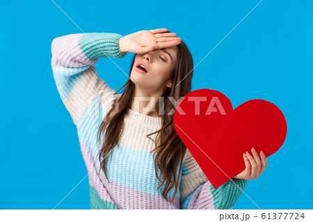 Affection, passion and relationship concept. Attractive romantic woman in winter sweater, sighing with hand on forehead, close eyes, holding big red heart, losing her mind from love, blue background 61377724
