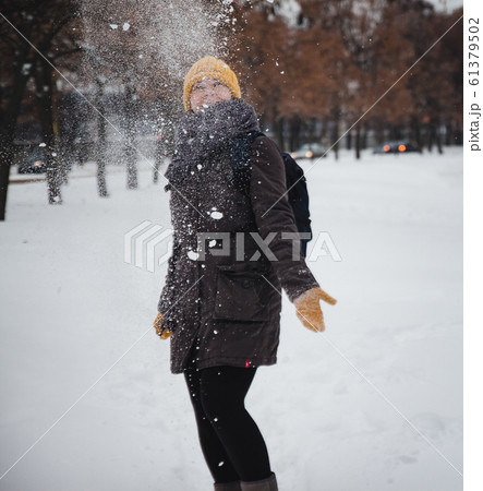 Happy young european woman in a yellow knitted hat and mittens with a backpack, laughs under the Happy young european woman in a yellow knitted hat and mittens with a backpack, laughs under the 61379502