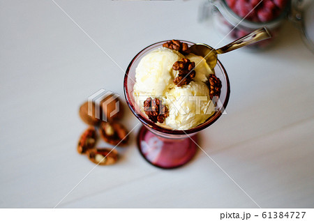 Creamy ice cream with honey and walnuts. Served in a bowl with ice cream, garnished with walnuts and honey. On the table is a jar with dried strawberries, a spoon and a walnut. 61384727