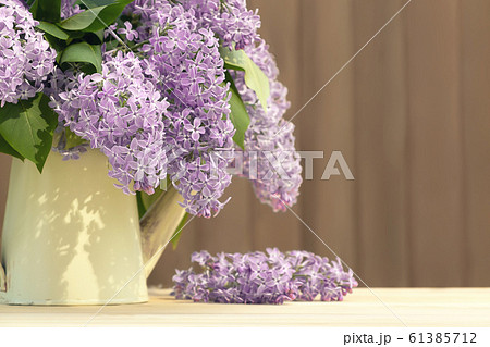 Vase in the form of an old vintage watering can with a bouquet of lilacs on table on a wooden background Vase in the form of an old vintage watering can with a bouquet of lilacs on table on a wooden background 61385712