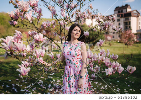 Charming girl stand by the beautiful pink magnolia tree outside. Gorgeous lady 61386102