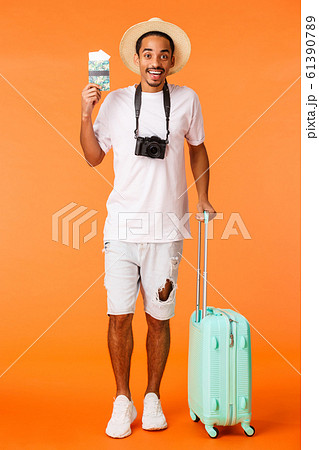 Full-length vertical shot african american happy boyfriend bought two tickets holidays luxury resort, holding luggage ready travel, standing airport terminal with passport, orange background Full-length vertical shot african american happy boyfriend bought two tickets holidays luxury resort, holding luggage ready travel, standing airport terminal with passport, orange background 61390789