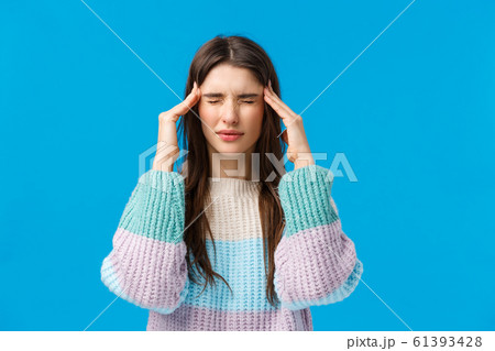Health, doctor, medicine concept. Waist-up portrait young woman feeling unwell, suffering headache, touching temples, squinting from pain and headache, standing blue background feeling bad Health, doctor, medicine concept. Waist-up portrait young woman feeling unwell, suffering headache, touching temples, squinting from pain and headache, standing blue background feeling bad 61393428
