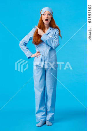 Full-length vertical shot excited and intrigued cheerful redhead female in nightwear and sleep mask, open mouth saying wow, have you seen it, pointing upper left corner amazed, blue background Full-length vertical shot excited and intrigued cheerful redhead female in nightwear and sleep mask, open mouth saying wow, have you seen it, pointing upper left corner amazed, blue background 61395309