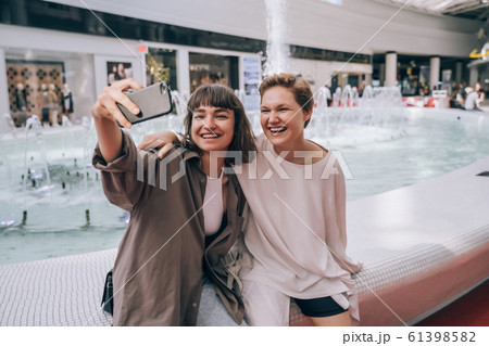 Two girls take a selfie in the mall, a fountain in the background 61398582