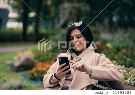 Happy girl using a smart phone in a city park sitting on a bench Happy girl using a smart phone in a city park sitting on a bench 61398683