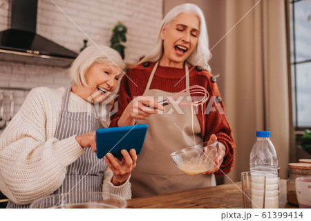 Grey-haired smiling lady in apron showing something on her smartphone 61399414