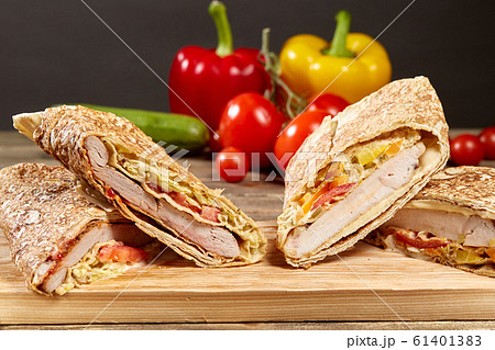 Shawarma chicken roll in a pita with fresh vegetables and cream sauce on wooden background. Selective focus 61401383
