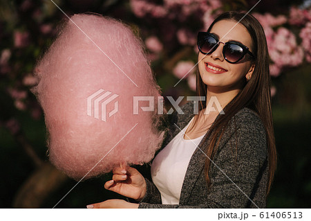 Close up portrait of attractive young girl eating cotton candy in front of pink sakura tree 61406513