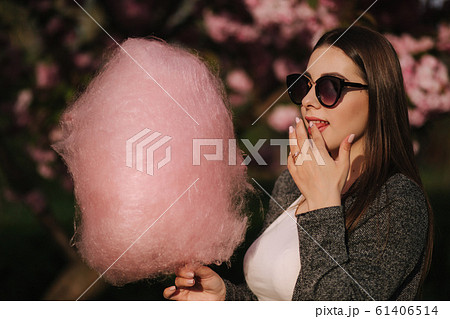 Close up portrait of attractive young girl eating cotton candy in front of pink sakura tree 61406514
