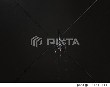 Four people rowing with an instructor in the background of black water 61410411