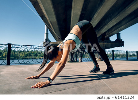 Young sporty woman doing yoga asana downward facing dog under industrial bridge 61411224