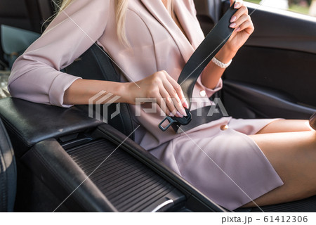 Close-up, girl in pink business suit, fastens her seat belt in the passenger compartment. Activation of airbags. In the summer in city. Close-up, girl in pink business suit, fastens her seat belt in the passenger compartment. Activation of airbags. In the summer in city. 61412306
